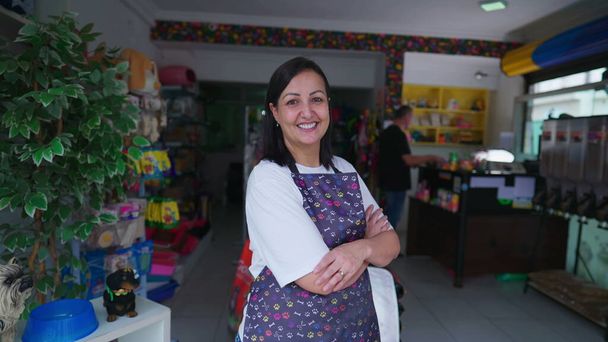 Boldog női vállalkozó PetShop mosolyogva, miközben keresztbe karját magabiztosan. Portré egy kisvállalkozóról, aki kötényt visel a bolt előtt. - Fotó, kép