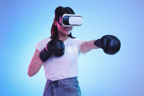 ИИ, виртуальная реальность и женщина-геймер бокса на синем фоне в студии для фитнеса или физических упражнений. Метаверс, спорт и тренировка с молодой женщиной-боксером, играющей в онлайн-игру фэнтези для здоровья. - Фото, изображение