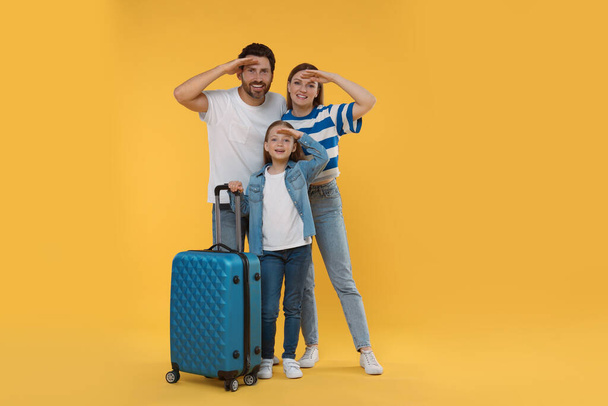 Happy family with green suitcase on orange background - Foto, Imagen