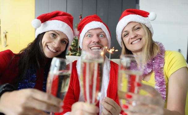 Mann und Frau in Weihnachtsmannhüten trinken Champagner und halten Wunderkerzen in den Händen. Neues Jahr mit Freunden und Familie - Foto, Bild