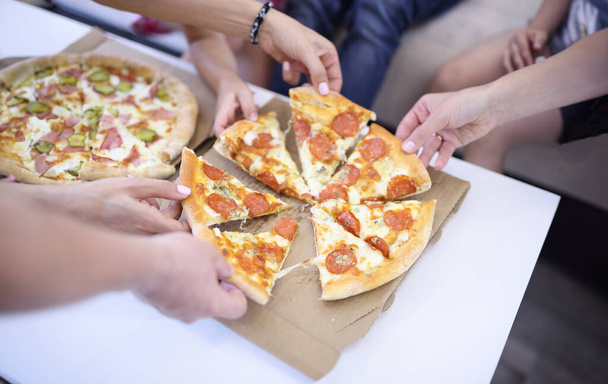 Auf dem Tisch liegen zwei offene Pizzaschachteln, jeder der Anwesenden nimmt ein Stück. Pizza-Lieferung im Stadtkonzept - Foto, Bild