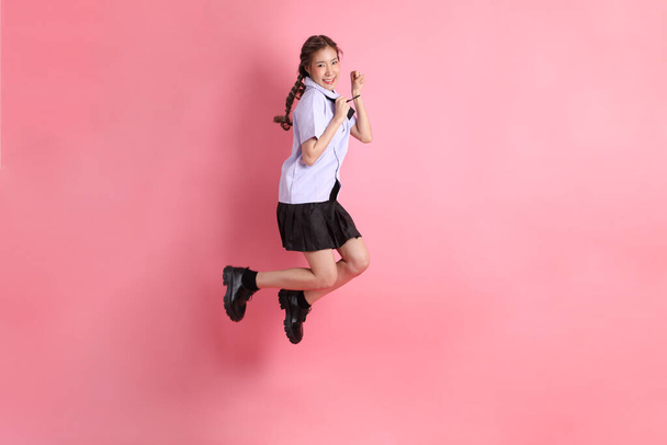 Азиатка в тайской студенческой форме, стоящая на розовом фоне. - Фото, изображение