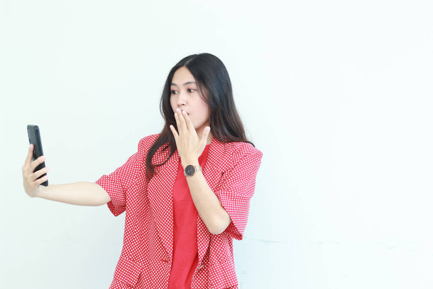 portrait de belle femme asiatique portant tenue rouge regardant téléphone mobile avec expression surprise isolé sur fond blanc. - Photo, image