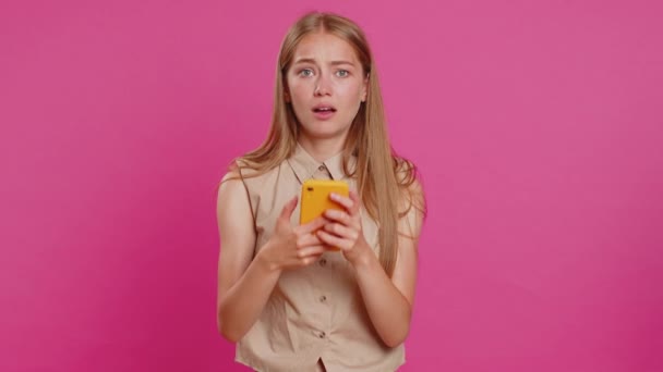 Woman use mobile phone smartphone typing browsing, loses becoming surprised sudden lottery results, bad fortune, loss, fail. Pretty blonde girl isolated alone on pink studio background, indoors - Footage, Video