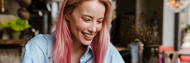 Young smiling woman with pink hair using mobile phone while sitting in cafe - Foto, Bild