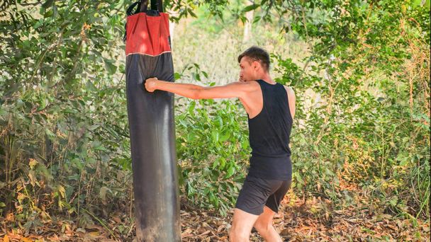 man is striking a punching bag with his left hand against the forest. High quality photo - Photo, Image