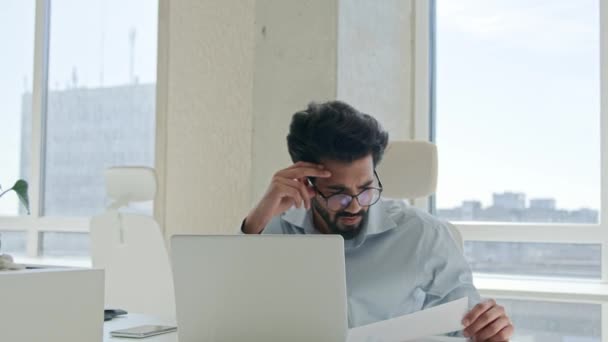 Stressful overwhelmed Arabian Indian man anxious businessman work on laptop check documents business commerce upset office manager accountant analyzing paper contract financial mistake debt problem - Footage, Video