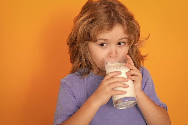 Органічне молоко. Прекрасна усміхнена дитина зі склянкою молока. Милий хлопчик у блакитній сорочці тримає склянку молока на жовтому ізольованому студійному фоні. Портрет смішного хлопчика з молочними вусами
 - Фото, зображення