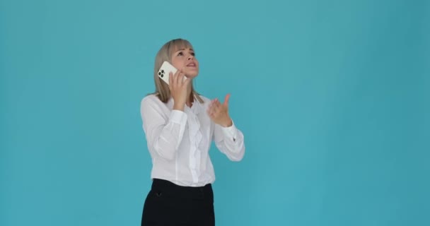 Geconcentreerde blanke vrouw wordt afgebeeld verzonken in een telefoongesprek tegen een serene blauwe achtergrond. Haar gefocuste uitdrukking duidt op haar diepe concentratie en aandacht voor de oproep.. - Video