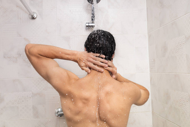 Visszapillantás egy zuhanyozó férfira. Vízcseppek hullanak rá a zuhanyfejből. - Fotó, kép