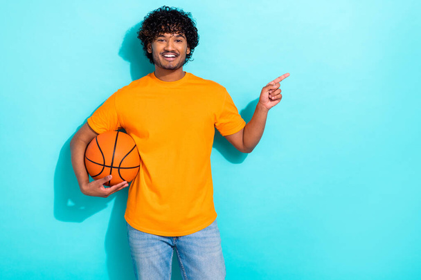 Photo of young sportsman player wear yellow t shirt hold basketball game direct finger empty space isolated on aquamarine color background. - Фото, изображение