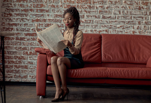 Modern iş kadını günlük haberleri okuyor, kırmızı koltukta otururken işe gitmeden önce sabah gazetesinde makale yazıyor. Rahatlamak için zihinsel bir hobi edinirken problem çözmeyi düşünmek. - Fotoğraf, Görsel