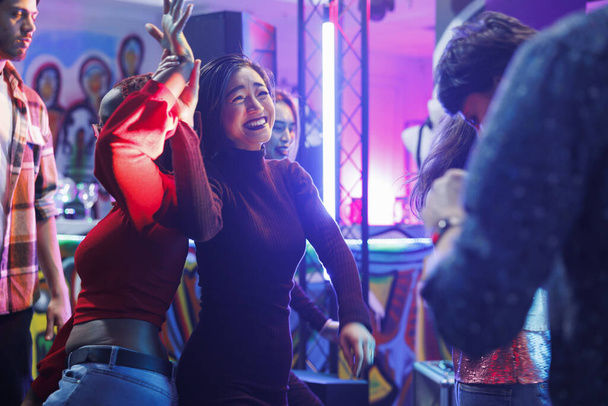 Cheerful smiling diverse women dancing together and laughing while partying and enjoying nightlife in club. Happy girlfriends having fun and celebrating on dancefloor in nightclub - Photo, Image