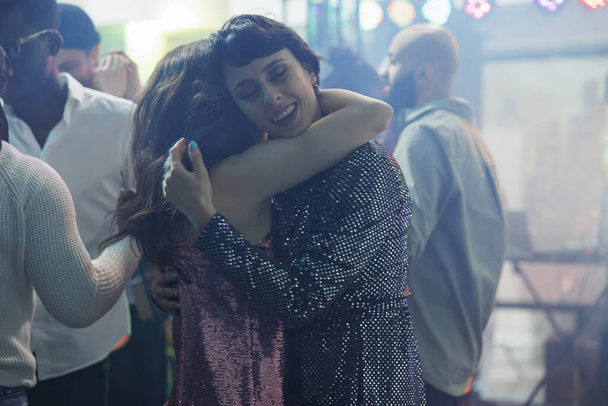 Gece kulübündeki disko partisine katılan genç kadınlar sarılıp dans ediyorlar. Dans pistinde kucaklaşan ve diskotek etkinliğinde rahatlayan romantik kız arkadaşlar. - Fotoğraf, Görsel