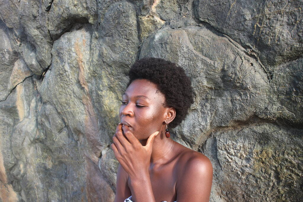 Afrikalı bir kadının büyüleyici portresi, afro saçı ve küpeleri kayalık arka planla uyumlu. - Fotoğraf, Görsel