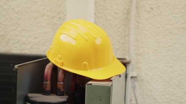 Extreme close up of yellow safety hardhat on top of out of order external air conditioner unit in need of repair. Protective professional engineering gear left on opened HVAC system - Footage, Video