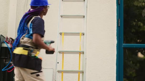 屋上エアコンのメンテナンスを行うために折りたたみ梯子を登る技術的な機器を持つプロのユニフォームのアフリカ系アメリカ人専門家. コンデンサーの点検に委託された訓練されたエンジニア - 映像、動画