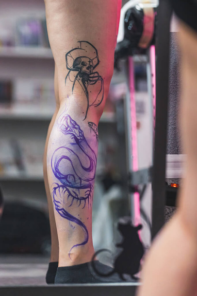 Vrije hand tatoeage techniek. Cliënt staat en toont haar been tatoeage proces aan de camera. Wazige achtergrond. Hoge kwaliteit foto - Foto, afbeelding