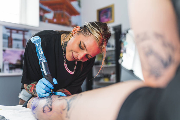 Feliz artista profesional del tatuaje hace un tatuaje en el estudio, en su pierna favorita de clientes femeninos. Foto de alta calidad - Foto, Imagen