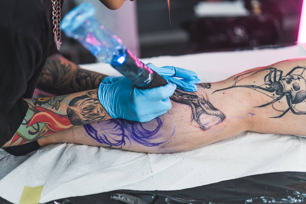 Tatuointi taiteilija hänen työssään. Lähikuva muotokuva osoittaa hygieeninen ja ammatillinen tatuointi päätöksenteossa. Asiakkaiden jalka on tatuoitu. Laadukas kuva - Valokuva, kuva