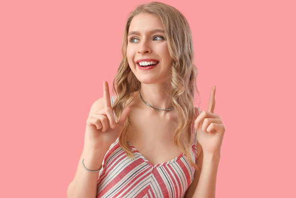 Young woman pointing at something on pink background - Photo, Image