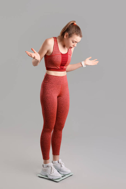 Összezavarodott fiatal nő méri súlyát mérlegen szürke háttér - Fotó, kép