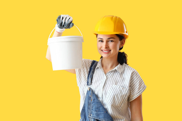 Женский декоратор с ведром краски на желтом фоне - Фото, изображение