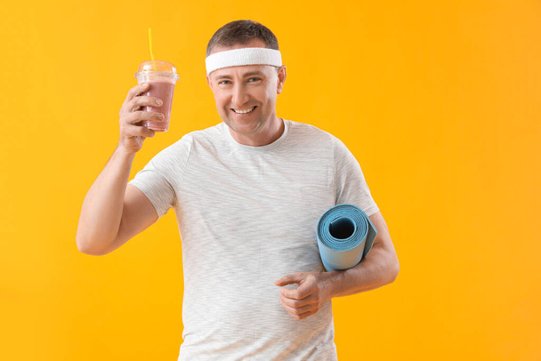 Sportos érett férfi üveg gyümölcs smoothie és fitness mat sárga alapon - Fotó, kép