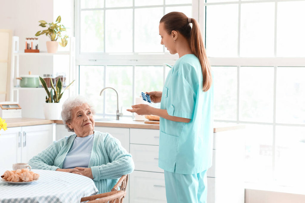 Vrouwelijke verzorger geven pillen aan senior vrouw in de keuken - Foto, afbeelding