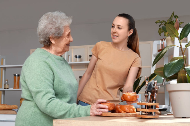 Starsza kobieta z wnuczką i smacznymi bułeczkami w kuchni - Zdjęcie, obraz