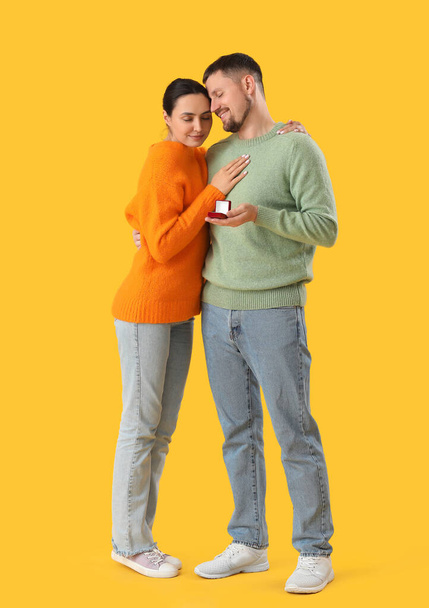 Young man proposing to his girlfriend on yellow background - Photo, image