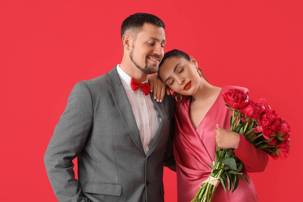 Happy engaged couple with flowers on red background - Photo, Image