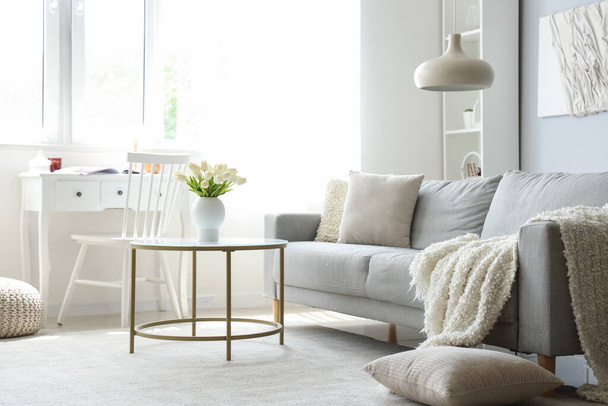 Accogliente divano grigio con morbida coperta e tavolino all'interno del luminoso soggiorno - Foto, immagini
