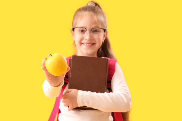 Μικρή μαθήτρια με βιβλία και μήλο σε κίτρινο φόντο - Φωτογραφία, εικόνα