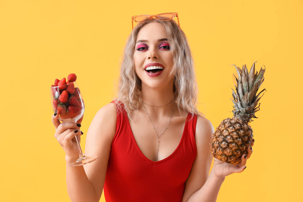 Junge Frau im Badeanzug mit Erdbeeren und Ananas auf gelbem Hintergrund - Foto, Bild