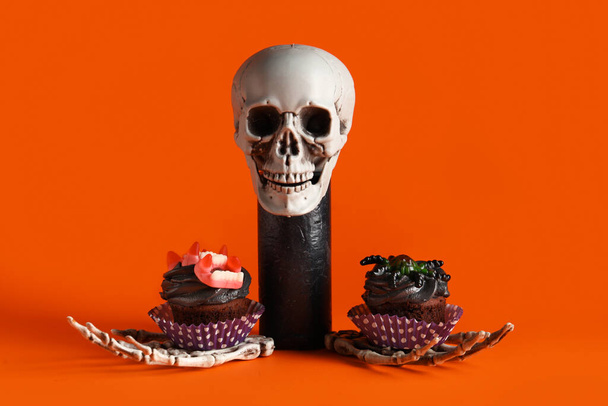 Композиція з черепом, руками скелета і смачними кексами на Хеллоуїн на червоному тлі - Фото, зображення