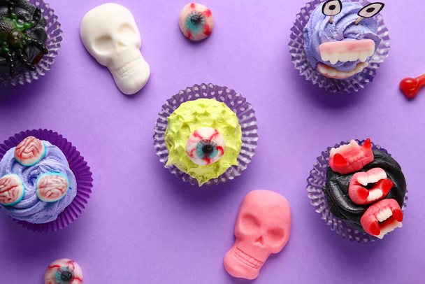 Composition with delicious Halloween cupcakes and candies on purple background, closeup - Photo, Image