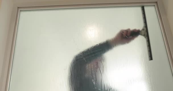 Een man plakt een matte coating op een glazen deur in een kliniek om de glazen deur ondoorzichtig te maken. Het aanbrengen van een matte coating op het glas. - Video