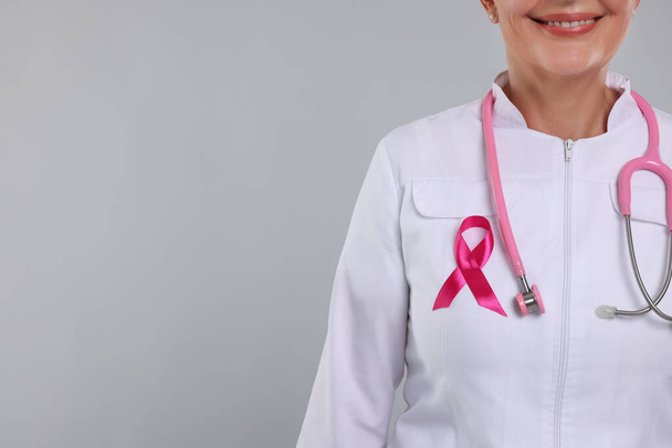 Doctor with pink ribbon and stethoscope on light grey background, closeup and space for text. Breast cancer awareness - Zdjęcie, obraz