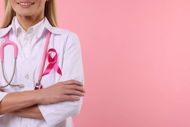 Doctor with pink ribbon and stethoscope on color background, closeup and space for text. Breast cancer awareness - Foto, imagen