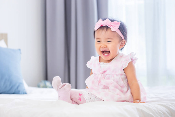 Azjatyckie dziecko maluch w ładny różowy sukienka jest uśmiechnięta siedząc na łóżku ze szczęściem dla zdrowego dziecka i urocze dziewczyny portret koncepcja - Zdjęcie, obraz