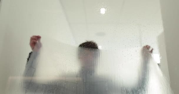 Een man plakt een matte coating op een glazen deur in een kliniek om de glazen deur ondoorzichtig te maken. Het aanbrengen van een matte coating op het glas. - Video
