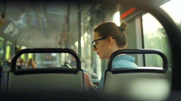 Openbaar vervoer. Vrouw met bril in tram met smartphone chatten en sms 'en met vrienden, achteraanzicht. Stad, stad, vervoer. - Video