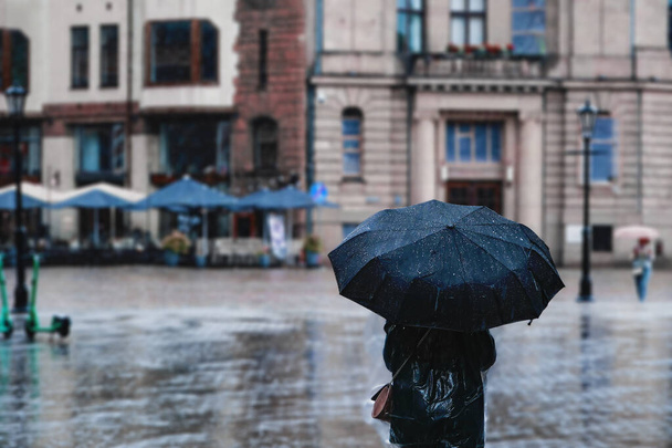 Een vrouw met een paraplu in de regen loopt langs de straat van de stad. Slecht weer. - Foto, afbeelding