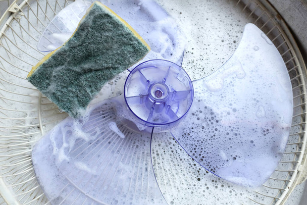 Κλείστε ένα ασιατικό νεαρή γυναίκα αποσυναρμολογεί τον ανεμιστήρα γεμάτη σκόνη για να καθαρίσει το φέρει ένα ηλεκτρικό ανεμιστήρα για να πλύνετε το νερό. τρίψτε με απορρυπαντικό. έννοια καθαρισμού νοικοκυριού - Φωτογραφία, εικόνα