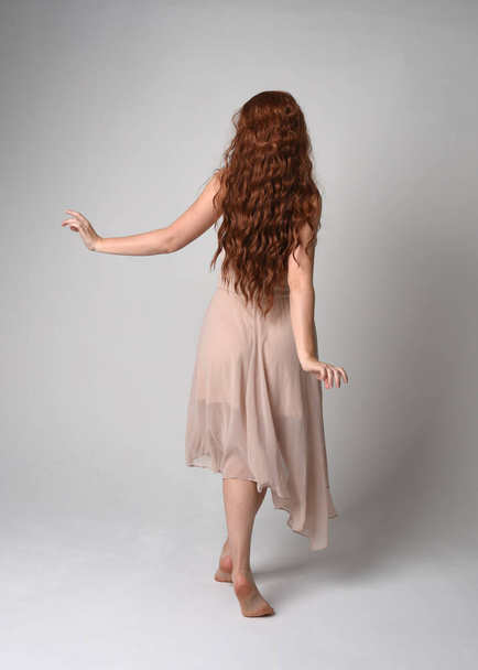 Portrait pleine longueur d'un beau modèle féminin avec de longs cheveux bruns portant une robe rose crème. pose de danse gracieuse, avec les mains gestuelles isolées sur fond de studio blanc. - Photo, image