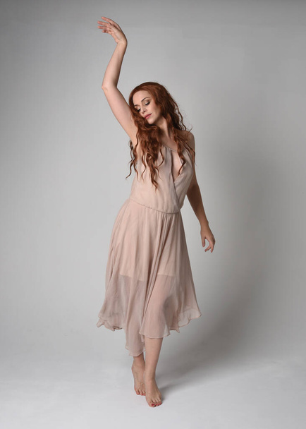 Volledig portret van mooi vrouwelijk model met lang brunette haar in een romige roze jurk. sierlijke dansende pose, met gebaren handen geïsoleerd op witte studio achtergrond. - Foto, afbeelding