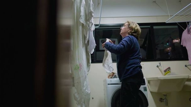 Donna anziana che tende a lavanderia su stendino, uno sguardo nella vita quotidiana. Scena di routine domestica di una donna anziana in pensione a casa. Candido e autentico - Foto, immagini