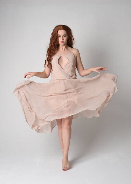 Ganzes Porträt der schönen weiblichen Modell mit langen brünetten Haaren trägt ein cremefarbenes Kleid Kleid. anmutige Tanzpose, mit gestenreichen Händen auf weißem Studiohintergrund. - Foto, Bild
