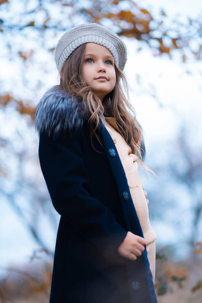 The low angle of a little girl with blue eyes is looking away. She is wearing a blue coat and gray hat - Photo, Image